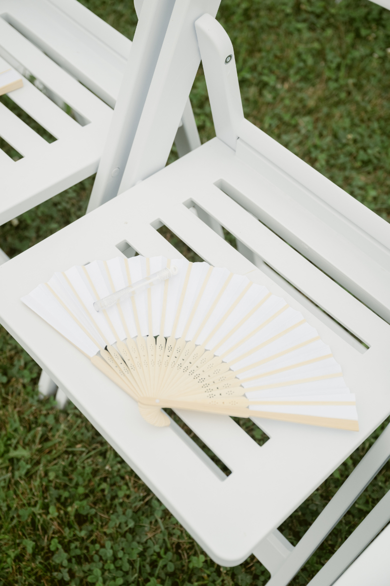 Paper fan placed on white ceremony chair, a thoughtful touch when designing guest experience for summer weddings.