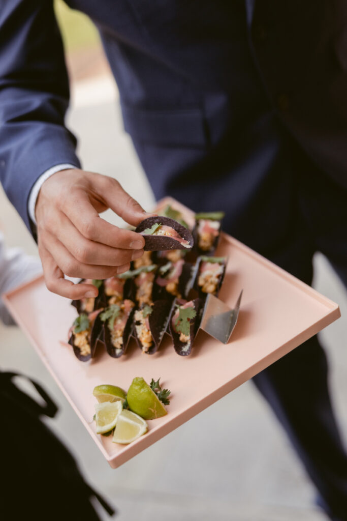 Guest selects a taco appetizer from a pink tray, a delicious detail in designing guest experience.
