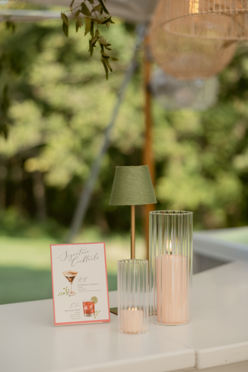 Signature cocktail sign displayed beside glowing candles and a small lamp on a modern white bar.