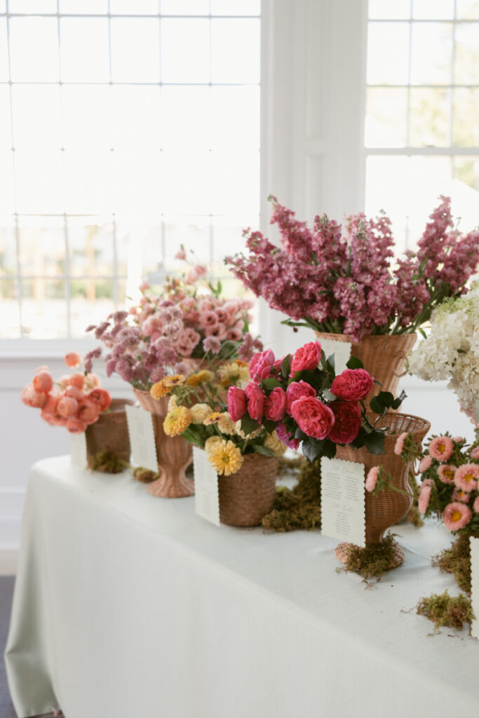 Floral seating chart display with vibrant flowers arranged in baskets, each holding guest names by table.