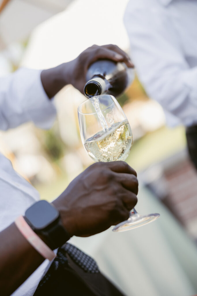 Guest pours white wine into a glass, a detail that reflects thoughtful wedding planning and designing guest experience.