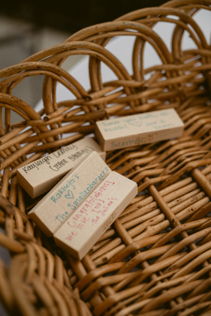 Close-up of handwritten messages on wooden Jenga blocks placed inside a woven basket guest book.
