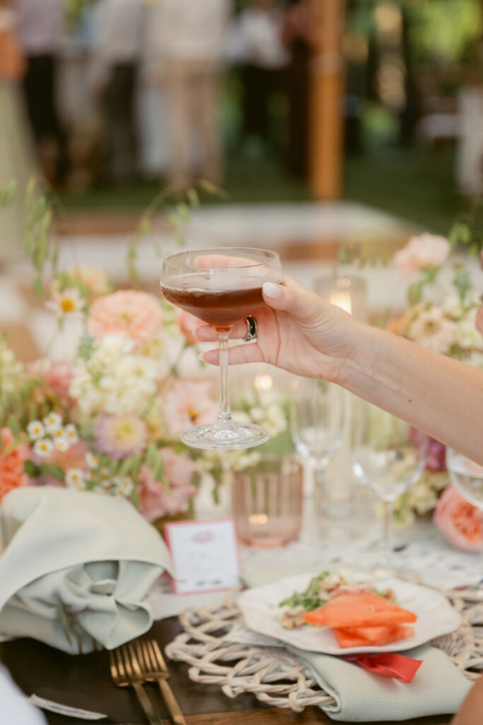 Guest raises cocktail over floral table setting, highlighting thoughtful details while designing guest experience.