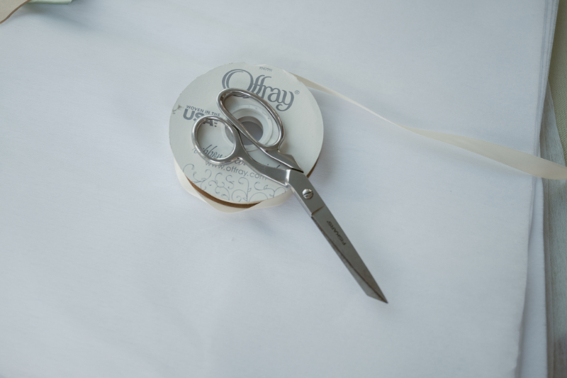 Silver scissors resting on a spool of white ribbon, ready for wedding day setup or decor prep.