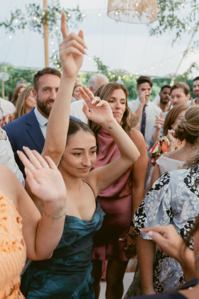 Wedding guests dancing under a tent with string lights during a lively outdoor reception celebration.