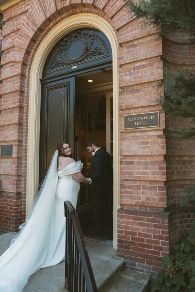 Bride looks back while entering Kingwood Hall with groom during their romantic Ohio garden wedding.