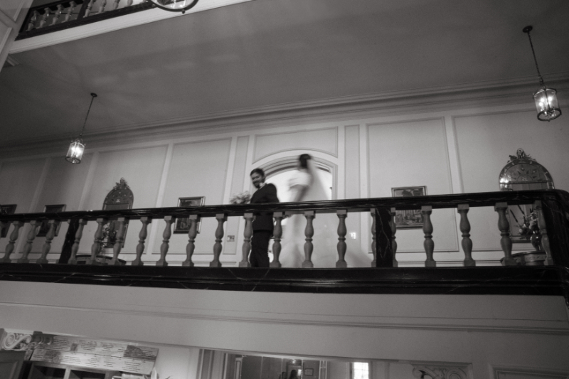 Bride and groom walk across an upper balcony inside Kingwood Hall during their Ohio garden wedding.