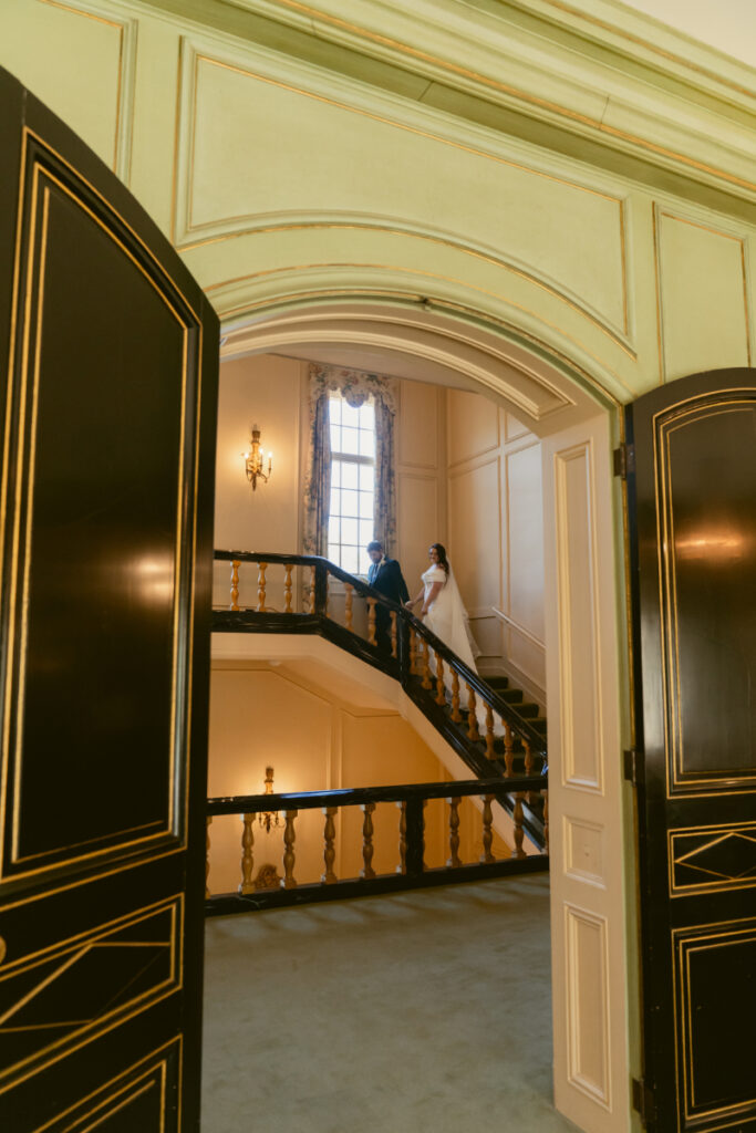 Bride and groom walk up grand staircase inside Kingwood Hall during their elegant Ohio garden wedding.