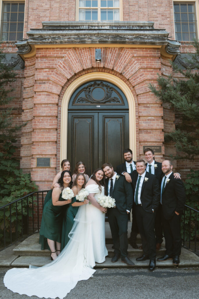 Wedding party poses together on mansion steps during sunny Ohio garden wedding at Kingwood Center Gardens.