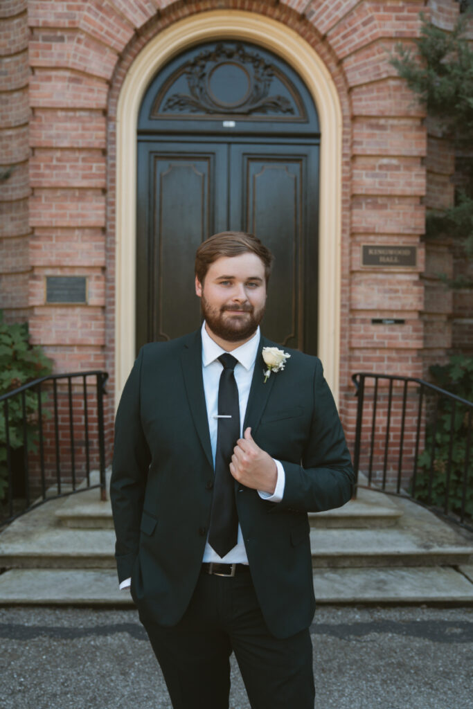 Groom standing confidently in front of historic mansion doors during Ohio garden wedding at Kingwood Hall.