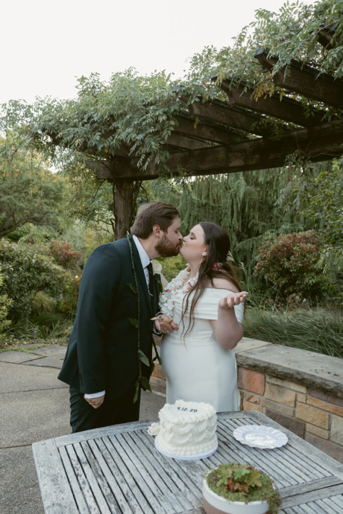 Bride and groom share a kiss after cutting cake during their romantic Ohio garden wedding.