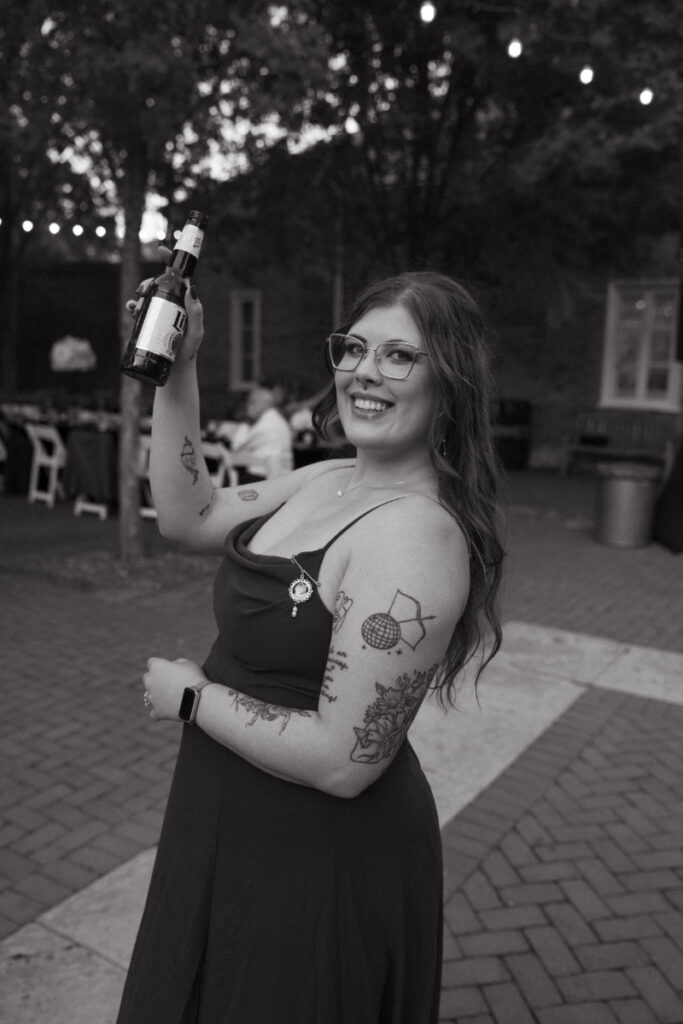 Guest raises a drink and smiles during the joyful Ohio garden wedding reception under string lights.