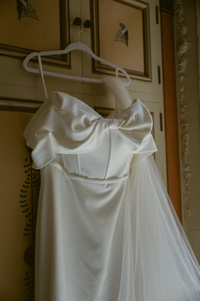 Off-the-shoulder wedding dress with structured bodice and veil hanging on a white hanger.