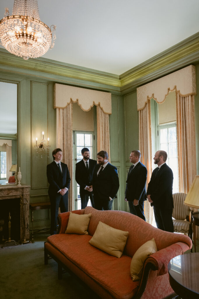 Groom and groomsmen talk in vintage room before Ohio garden wedding at Kingwood Center Gardens.