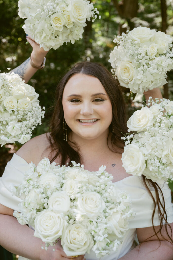 Bride smiling with white bouquets surrounding her during sunny outdoor portrait at Ohio garden wedding.
