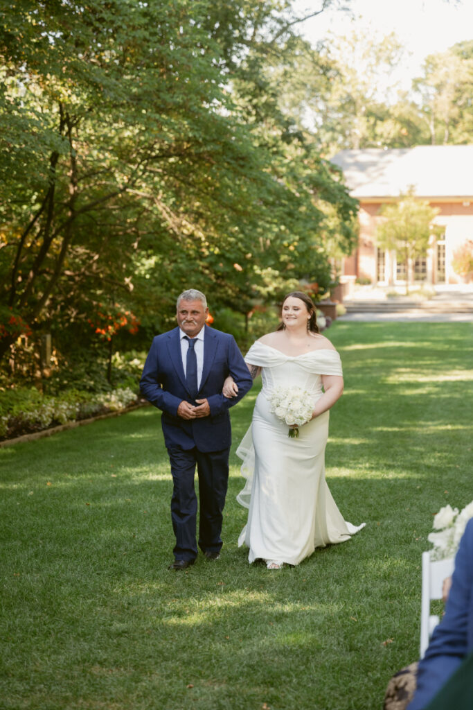Bride walks down grassy aisle with her father during outdoor Ohio garden wedding ceremony.