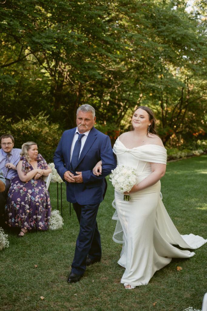 Bride smiles while walking down the aisle with her father during an outdoor Ohio garden wedding ceremony.