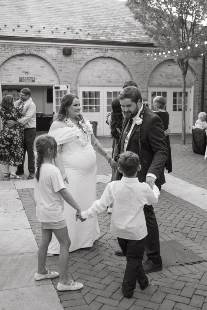 Bride and groom dance in a circle with children during joyful evening wedding reception.