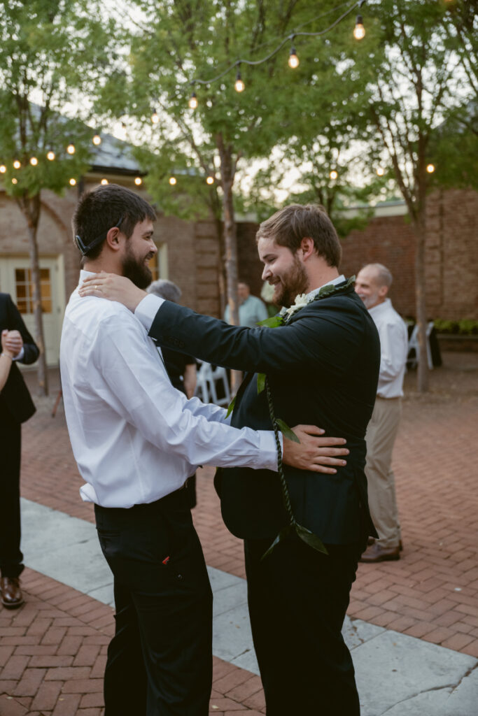 Two wedding guests smile and dance together during an outdoor evening reception under string lights.