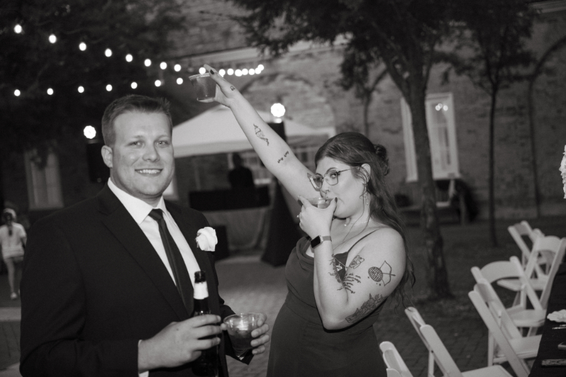Wedding guest raises a drink in celebration during a lively evening reception under string lights.