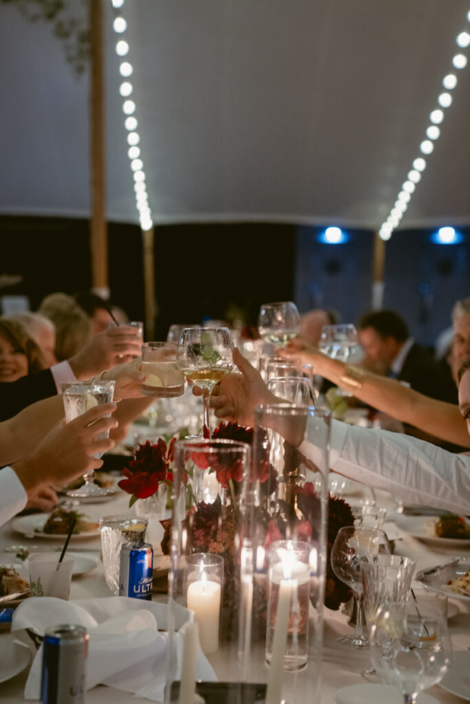 Guests raise glasses for a toast at a beautifully decorated reception table under a glowing tent.