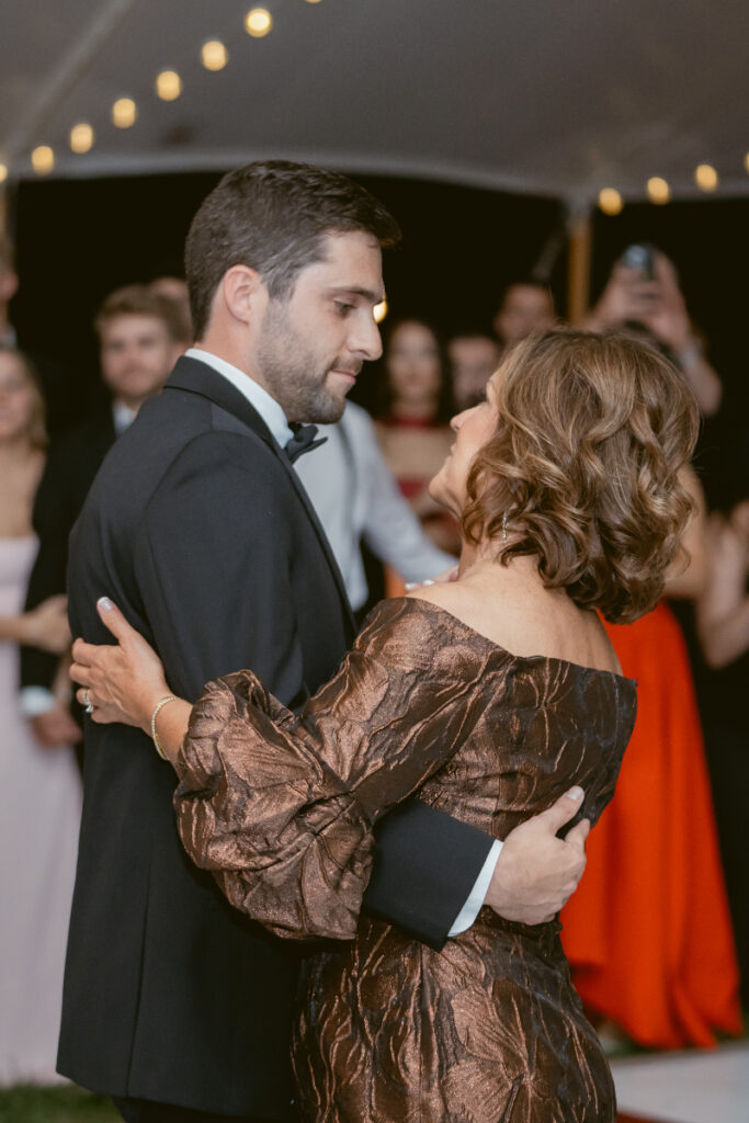 Groom shares a heartfelt dance with his mother under the tent, surrounded by watching guests.