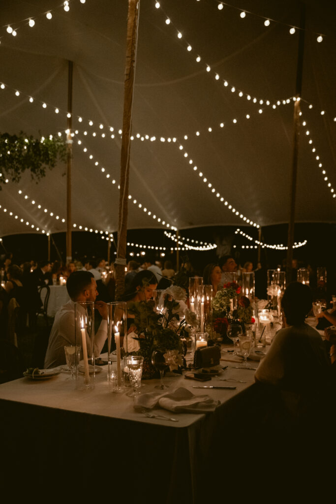 Candlelit outdoor wedding reception under a tent with string lights and elegant table decor at night.