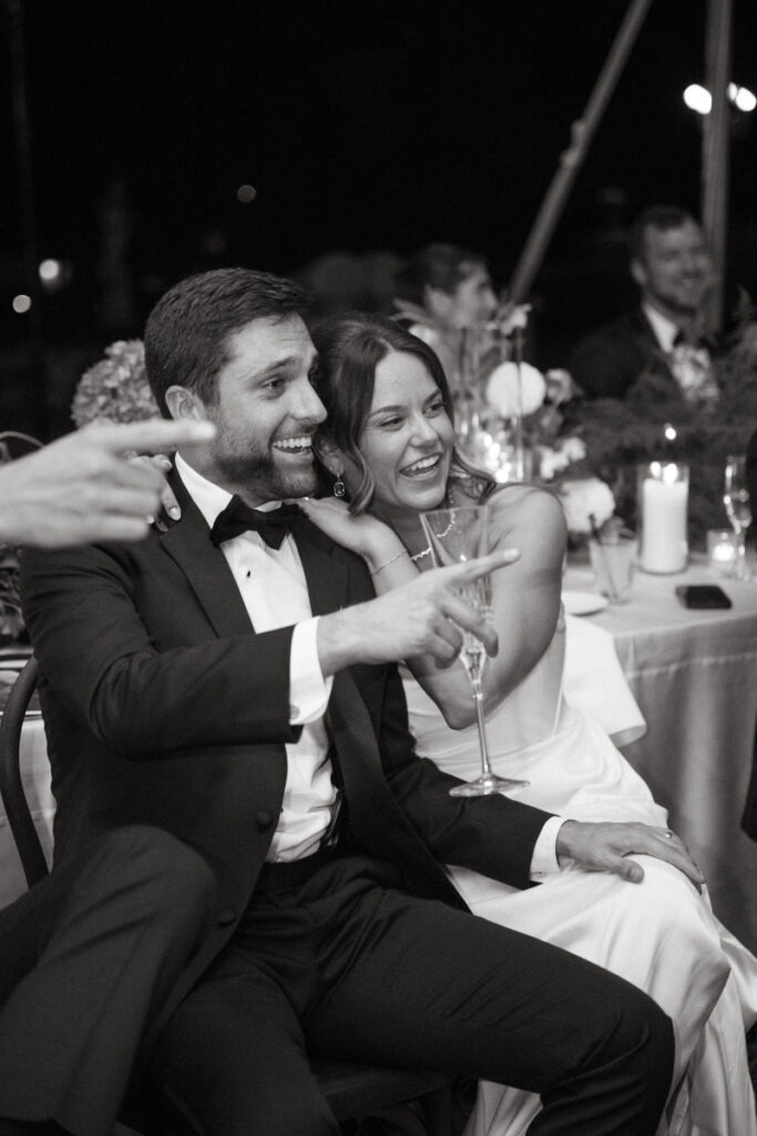 black and white photo of the bride and groom laughing and smiling while watching their guests on the dance floor
