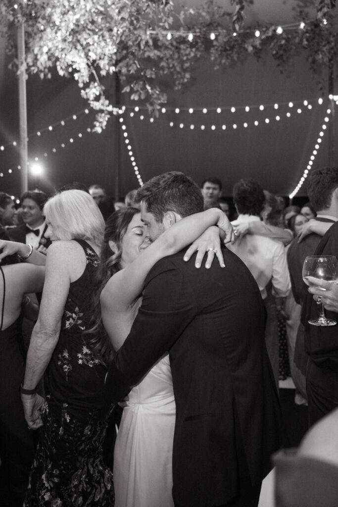 Bride and groom share a joyful embrace during their wedding reception under romantic string lights.