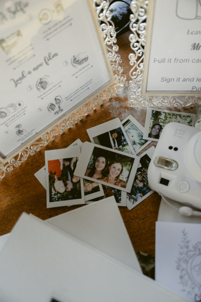 Stack of instant photos and camera at wedding guestbook table with decorative instruction signage.