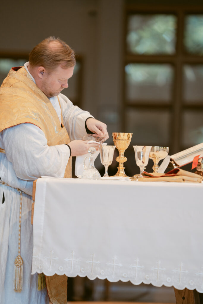 Priest preparing communion during Catholic ceremony before the couple’s Laurel Court wedding celebration.
