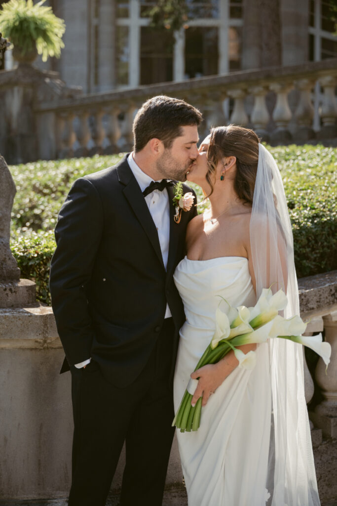 Bride and groom share a kiss holding calla lilies during elegant Laurel Court wedding celebration outdoors.