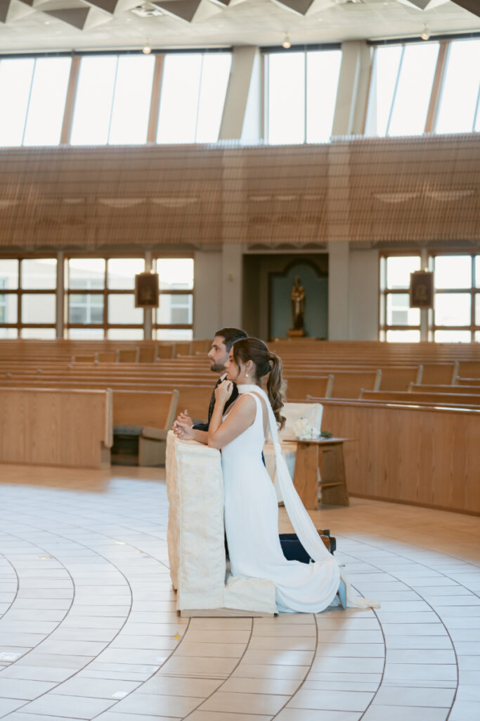 Bride and groom kneeling in prayer during Catholic ceremony before their Laurel Court wedding.