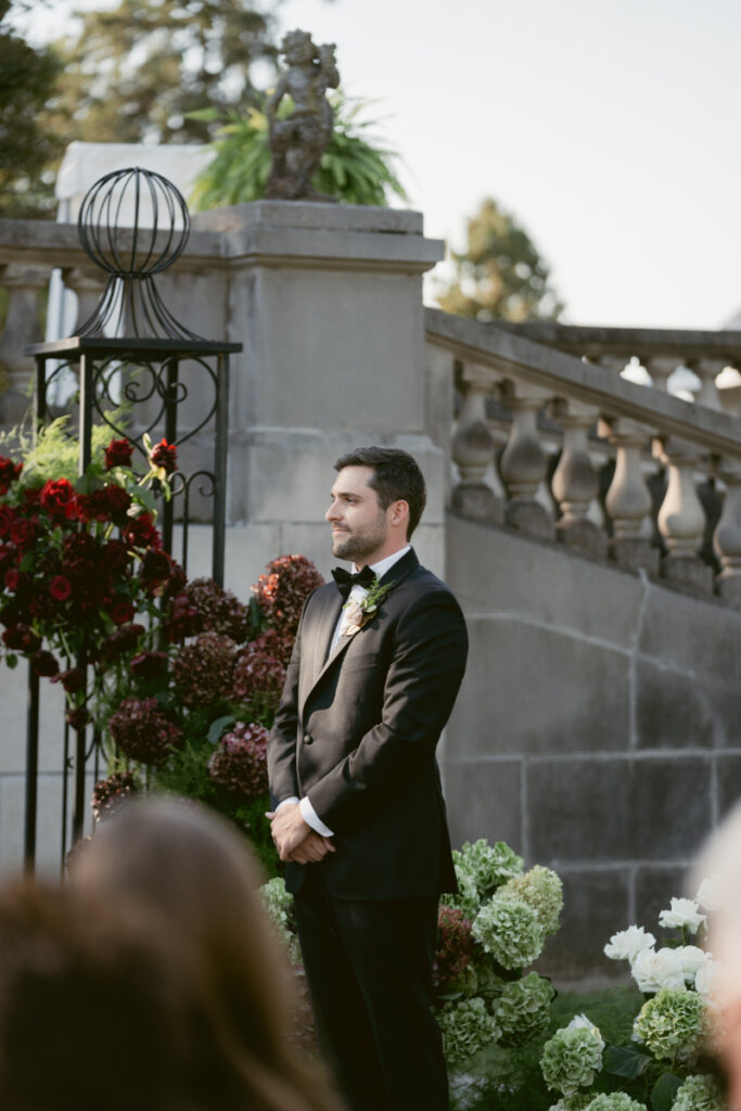 Groom stands at the altar, waiting with anticipation during outdoor wedding ceremony surrounded by flowers.