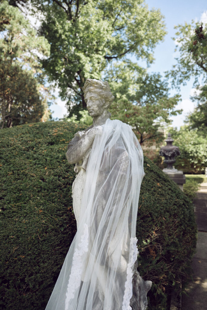 Bridal veil draped over garden statue during outdoor portraits at a Laurel Court wedding.