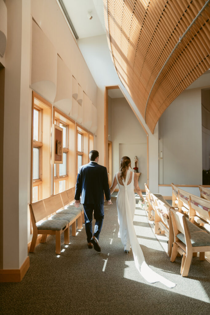 Bride and groom walking hand in hand through sunlit church hallway before their Laurel Court wedding.