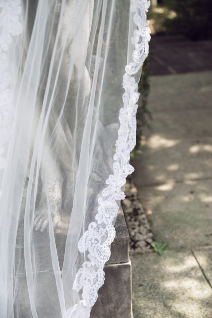 Close-up of lace-trimmed bridal veil draped over statue during a Laurel Court wedding.
