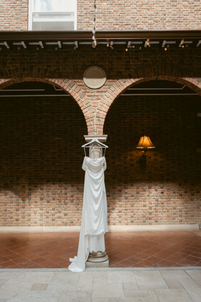 Wedding dress hanging on statue in courtyard during getting ready for a Laurel Court wedding.