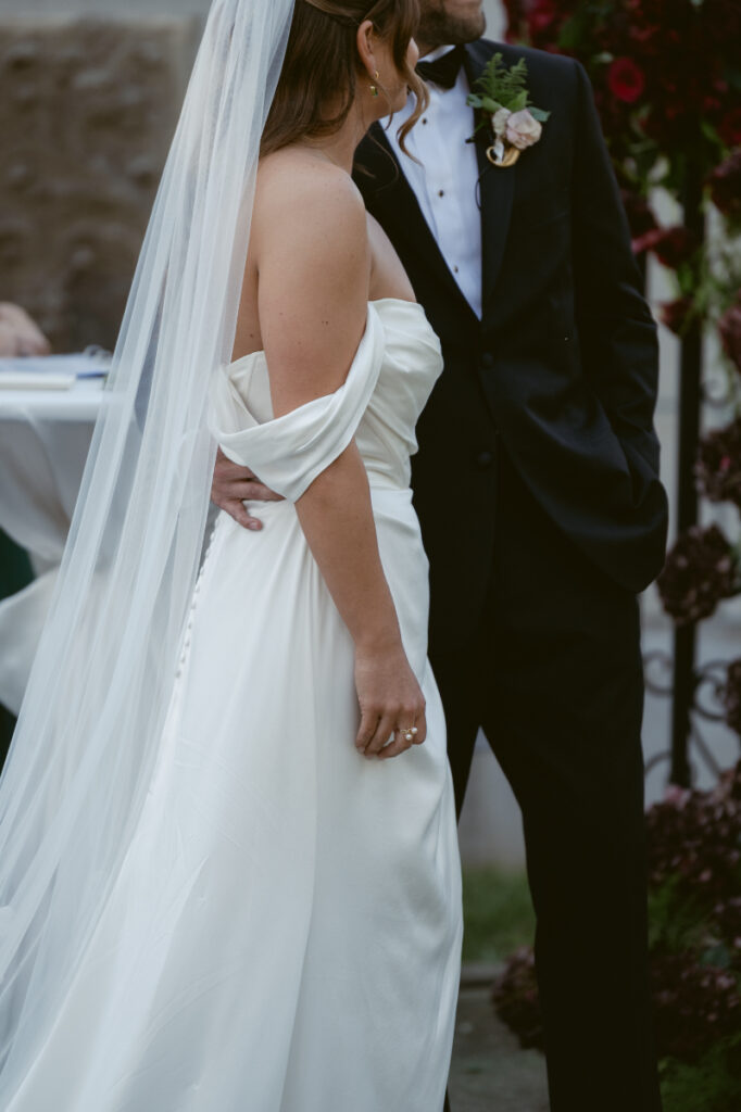 Close-up of bride and groom standing together during ceremony, his hand gently resting on her back.