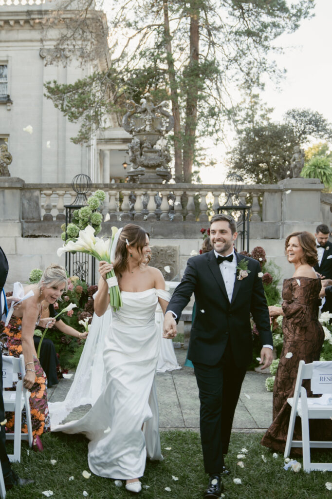 Bride and groom share a kiss at the altar as wedding guests applaud during outdoor ceremony.