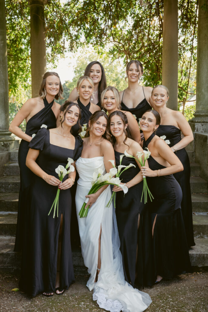 Bride surrounded by bridesmaids in black dresses holding calla lilies at Laurel Court wedding in Cincinnati.