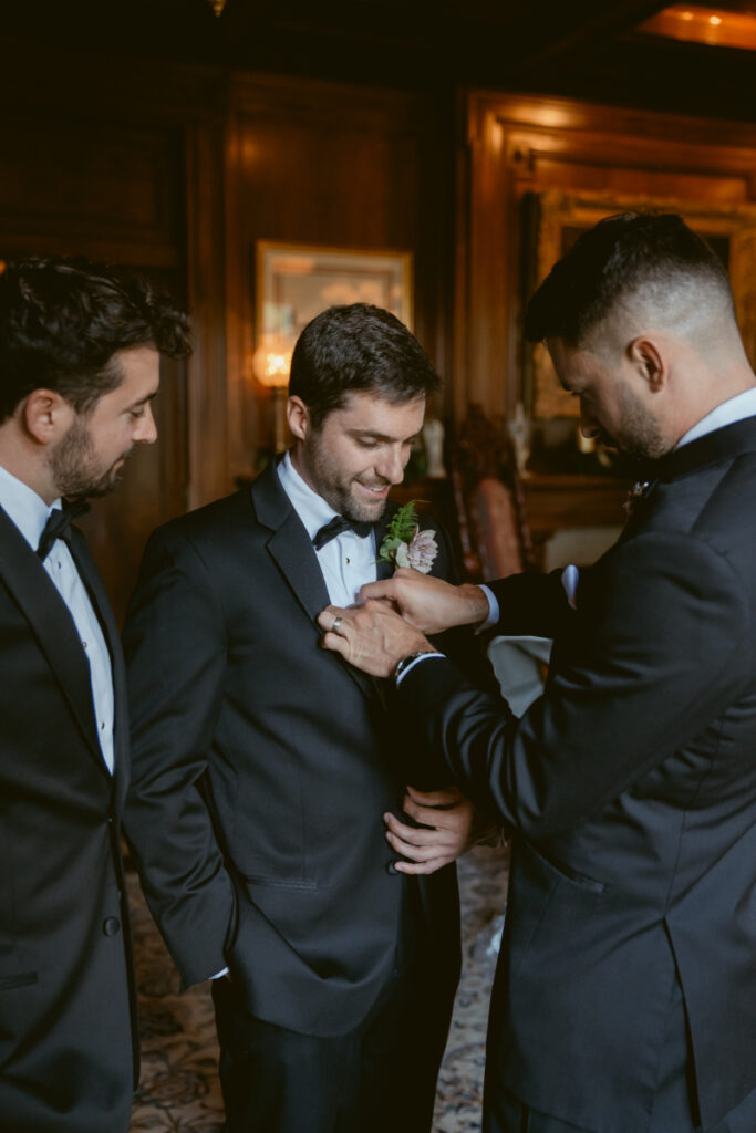 Groomsmen helping groom with boutonniere in library before his Laurel Court wedding ceremony.