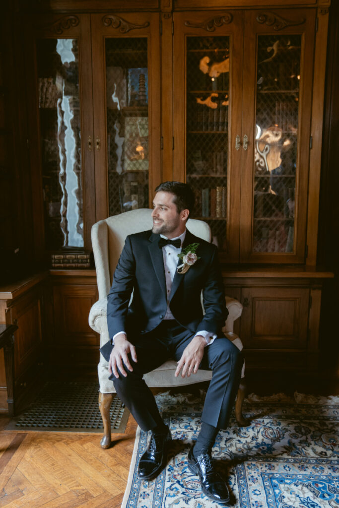 Groom sitting in library room, smiling before the ceremony at his Laurel Court wedding.