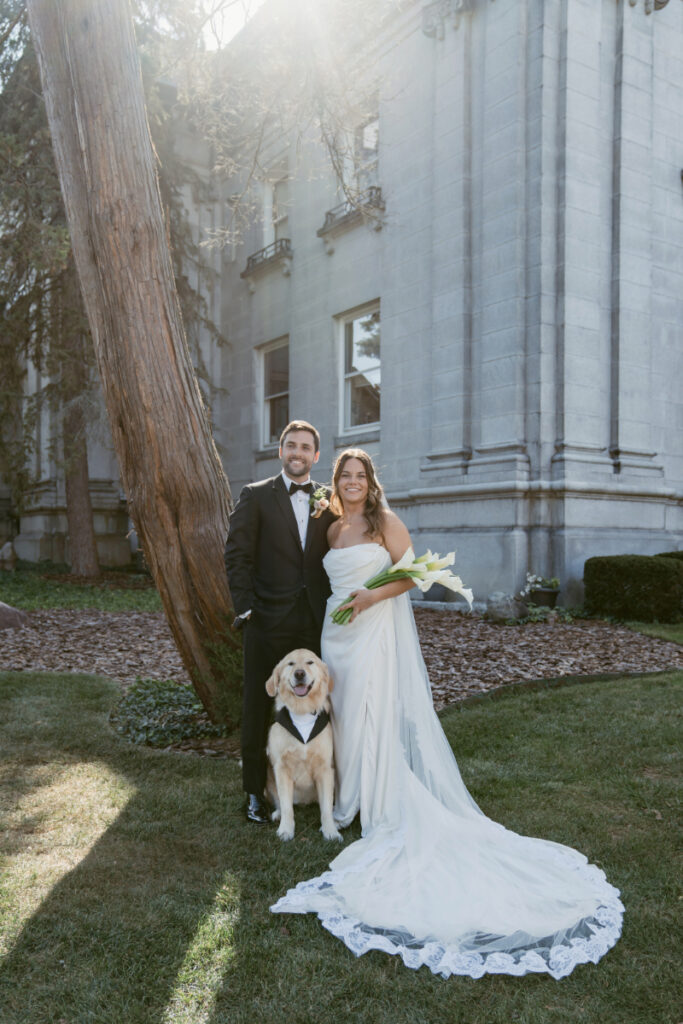Bride and groom with dog in tuxedo pose outside elegant Laurel Court wedding venue in Cincinnati.