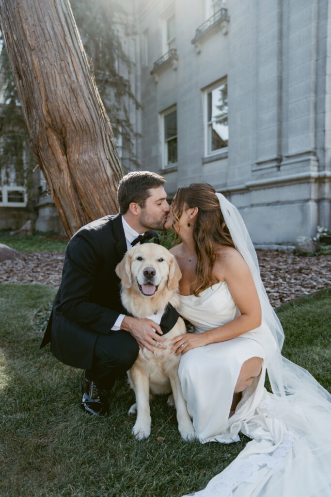 Bride and groom kiss while their dog in a tuxedo smiles at Laurel Court wedding venue in Cincinnati.