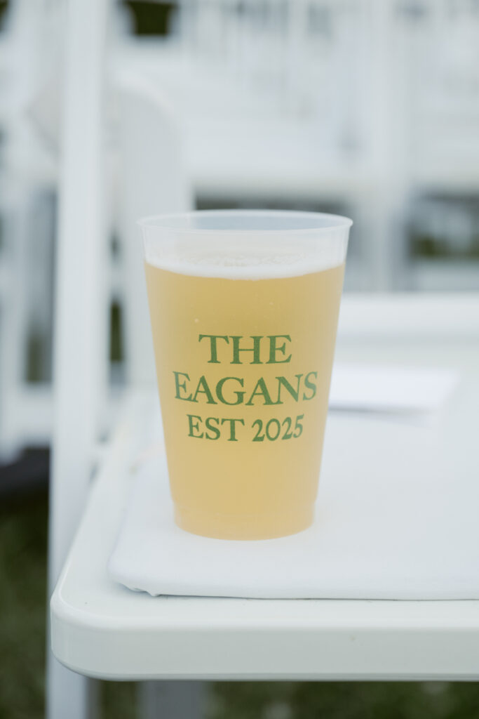 Personalized wedding cup with “The Eagans Est 2025” filled with drink, resting on white chair.