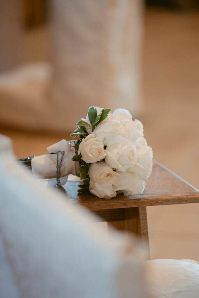 White rose bridal bouquet with rosary resting on pew during a Laurel Court wedding ceremony.