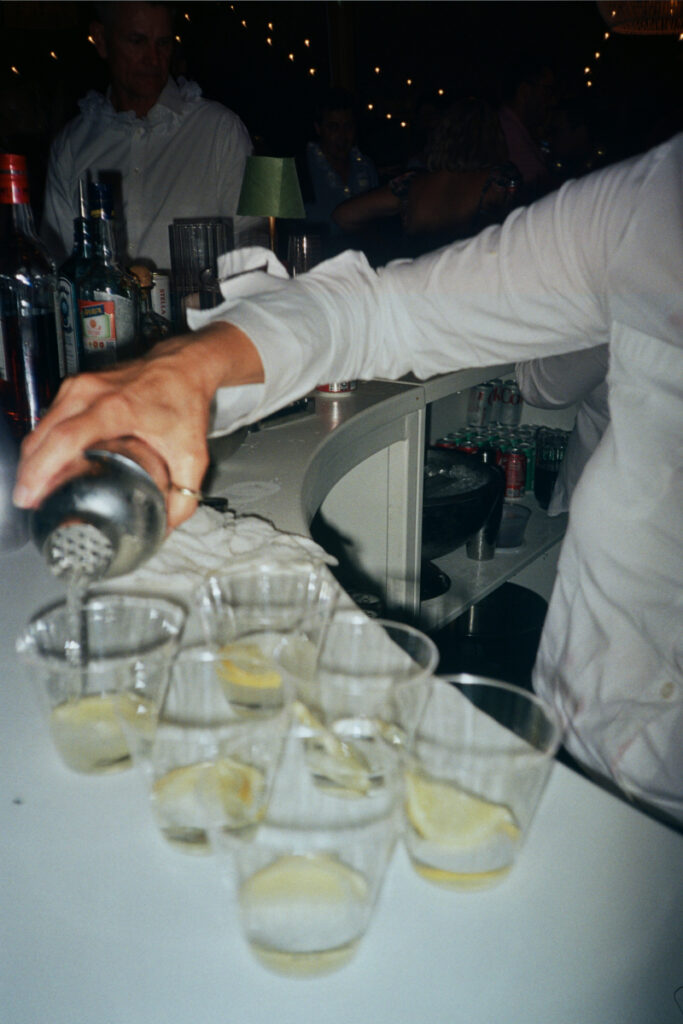 A bartender pours cocktails into clear cups, capturing the buzz and energy of the late-night celebration.