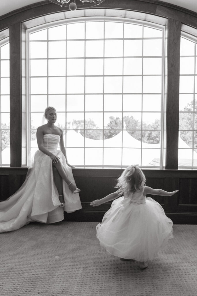 Flower girl twirls toward the bride in a quiet room—sweet Moments You Won’t See on Your Wedding Day.