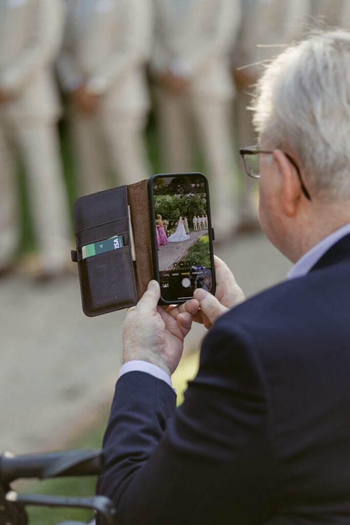 Guest captures the bride’s entrance on his phone—cherished Moments You Won’t See on Your Wedding Day.